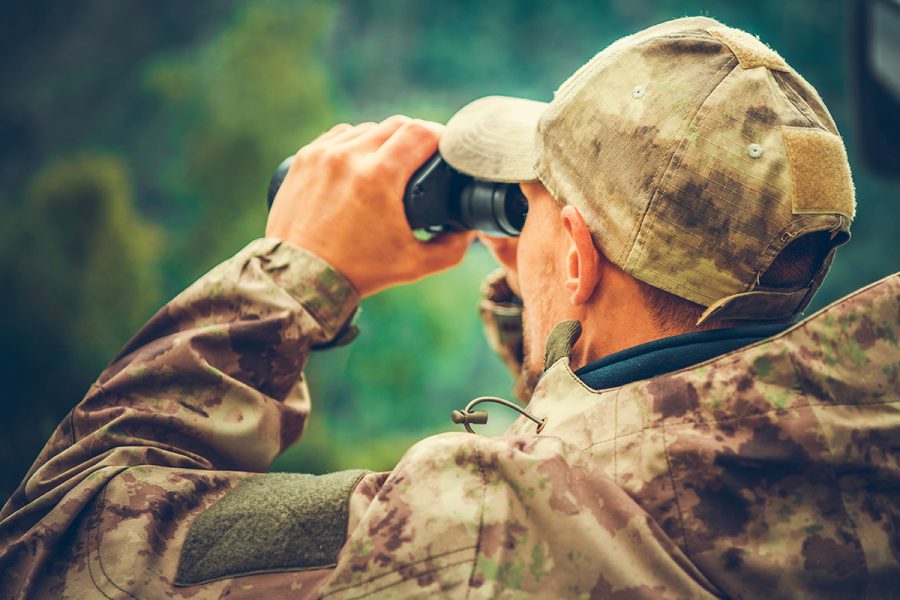 hunter looking through binoculars in the mountains